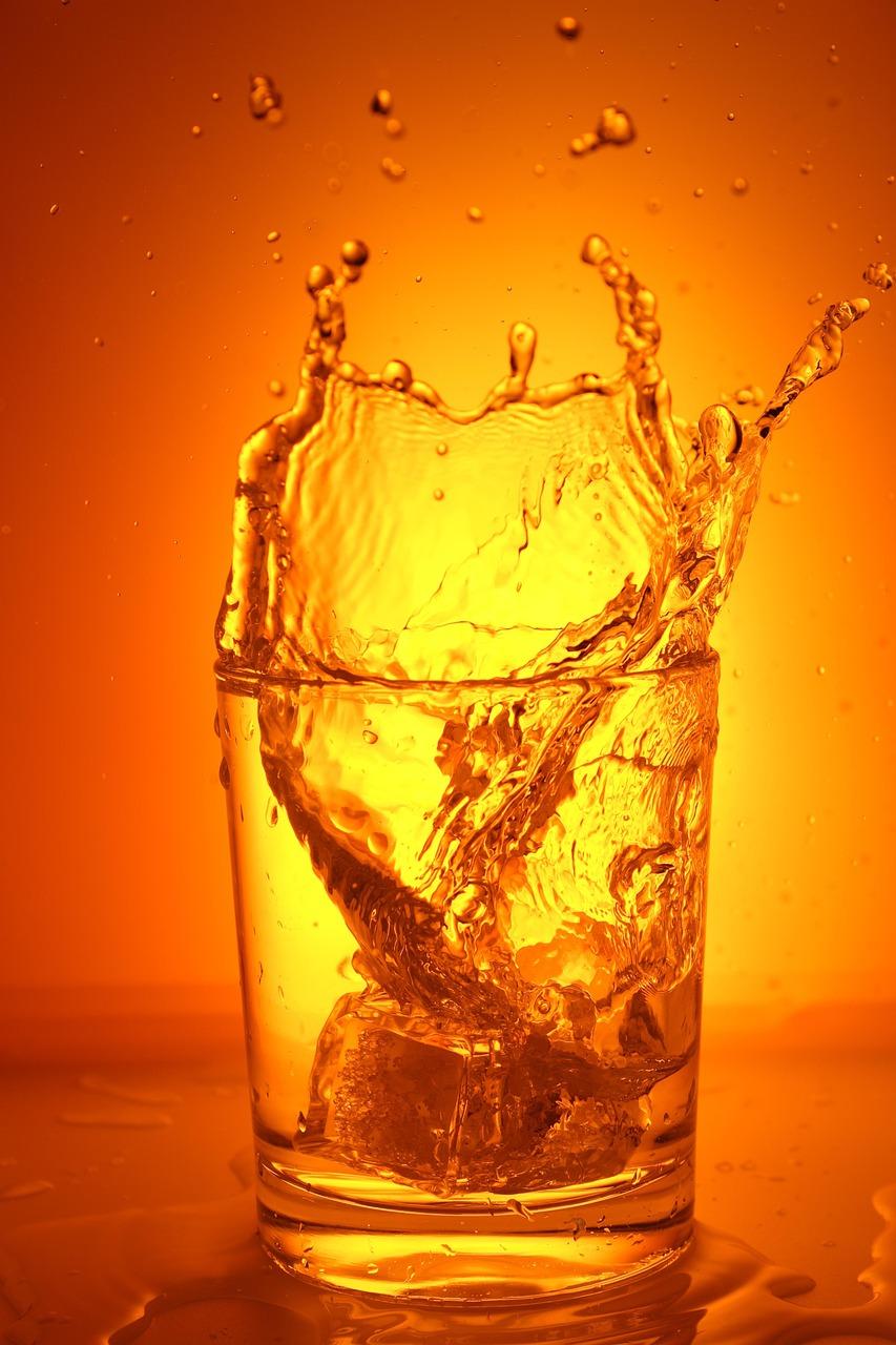 A glass of cold water with ice cubes resting on a table under bright summer sunshine