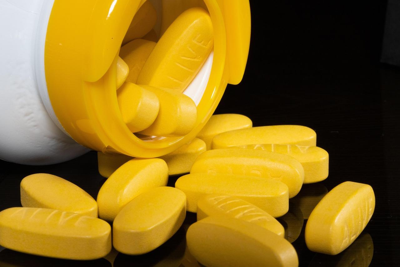 A prescription pill bottle and pharmaceutical tablets sitting beside a wooden mortar and pestle