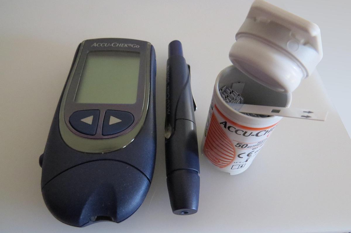 A glucometer kit with test strips and lancing device placed on a wooden desk