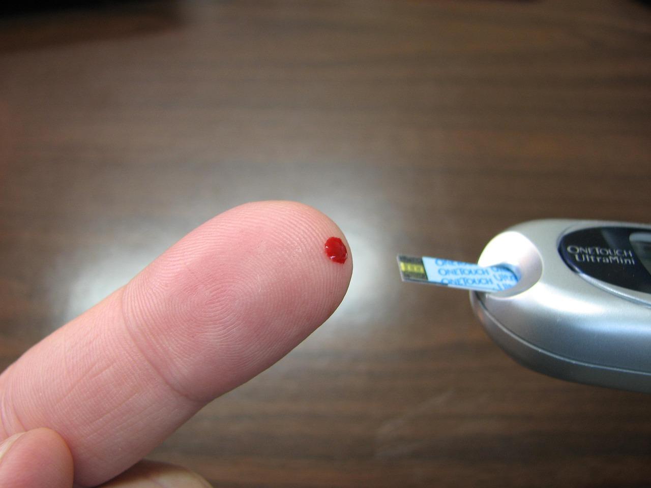 Hands carefully holding a lancing device and placing a drop of blood on a test strip