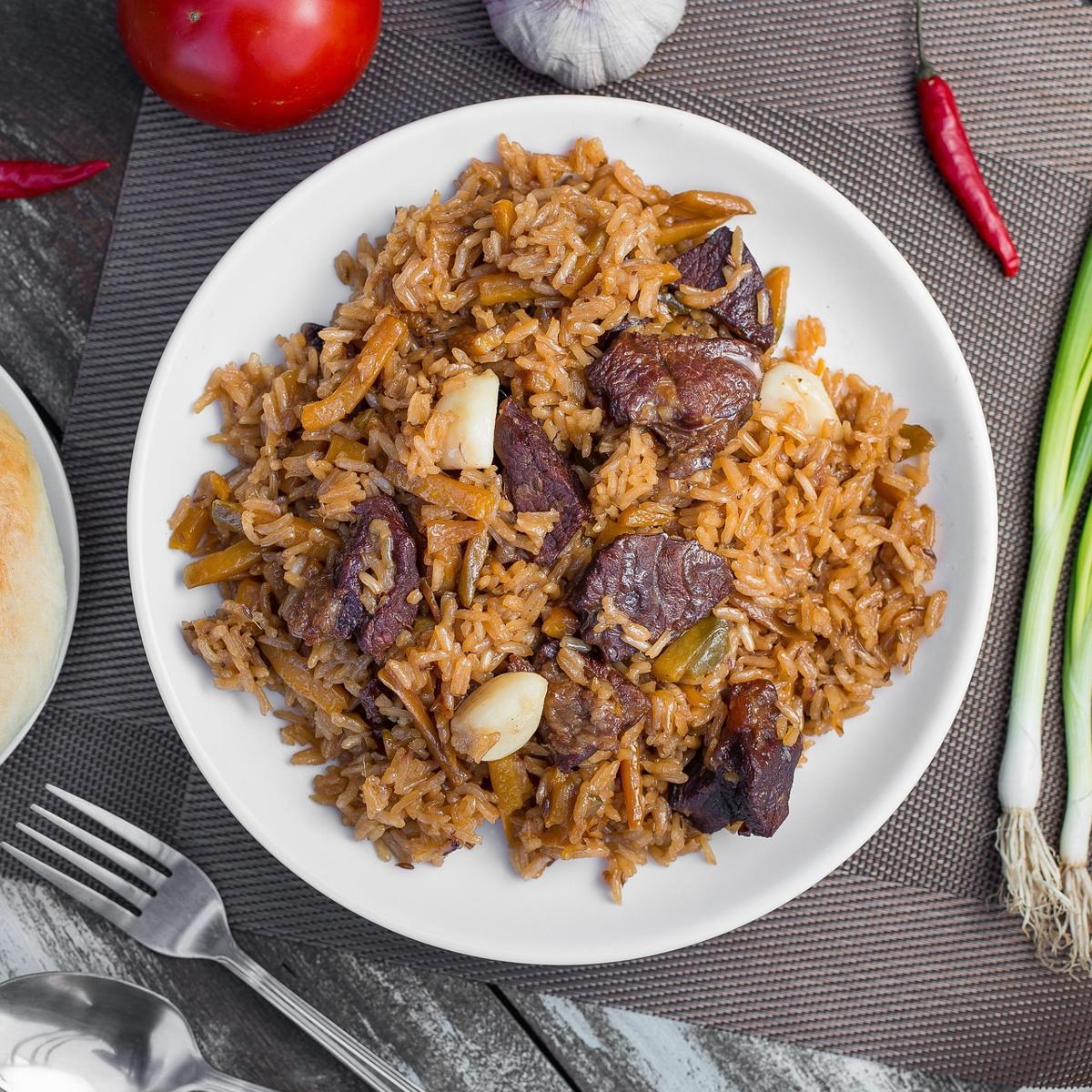 A pot of biryani being layered with rice, meat and vegetables at home