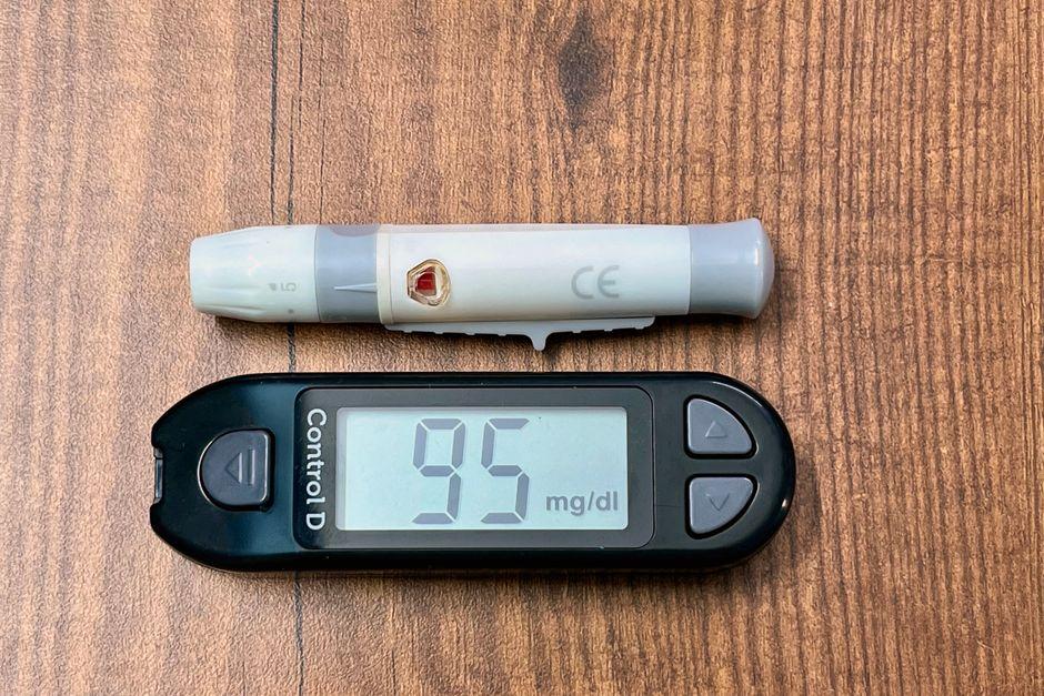 Close up of glucometer screen showing a reading with notepad and pen ready